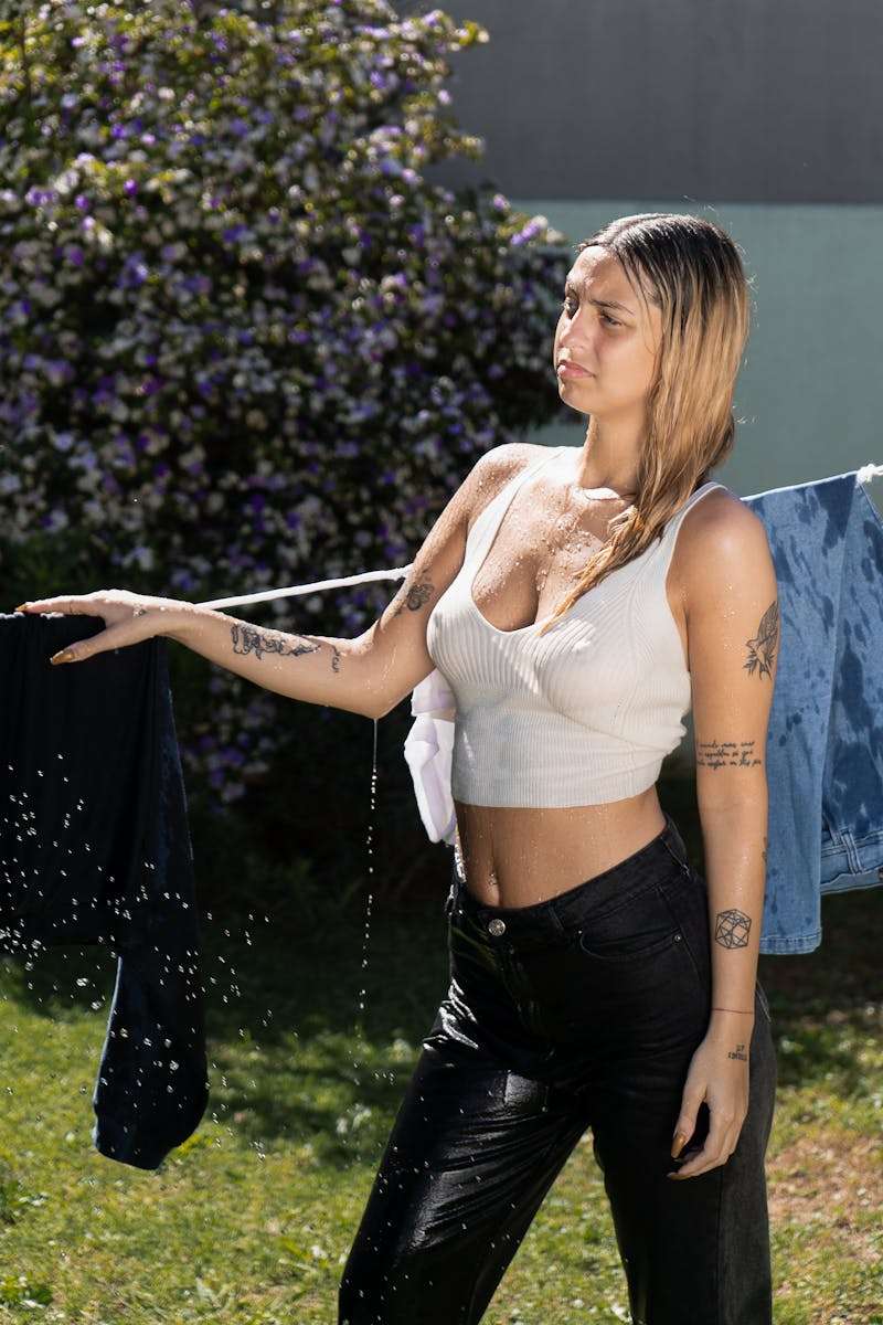 A woman in a white top and black pants is hanging clothes on a line