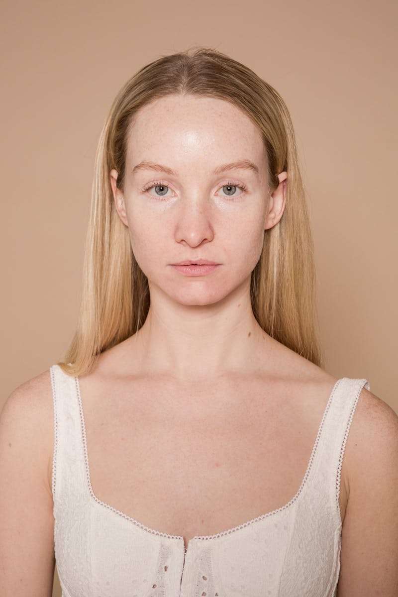 Emotionless female model with long hair showing natural skin looking at camera against beige background