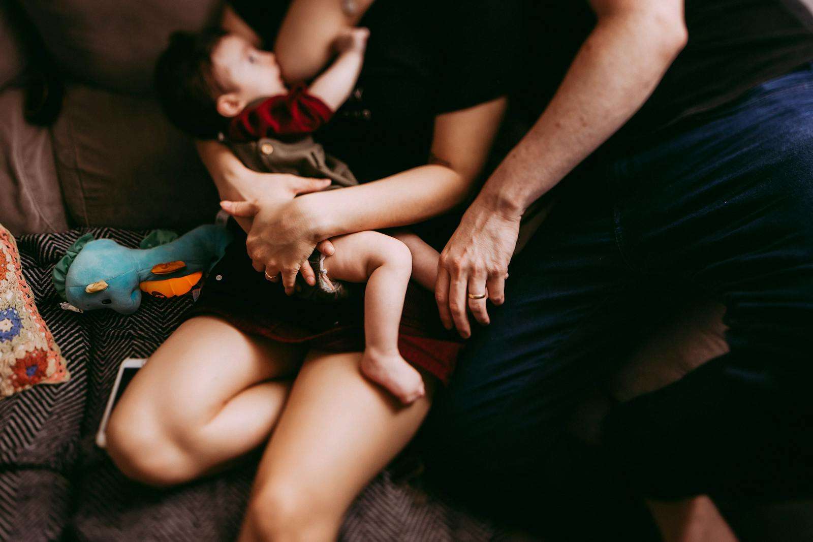 Crop mother breastfeeding baby near father