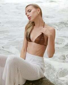 blonde woman in bikini and white pants sitting on sand
