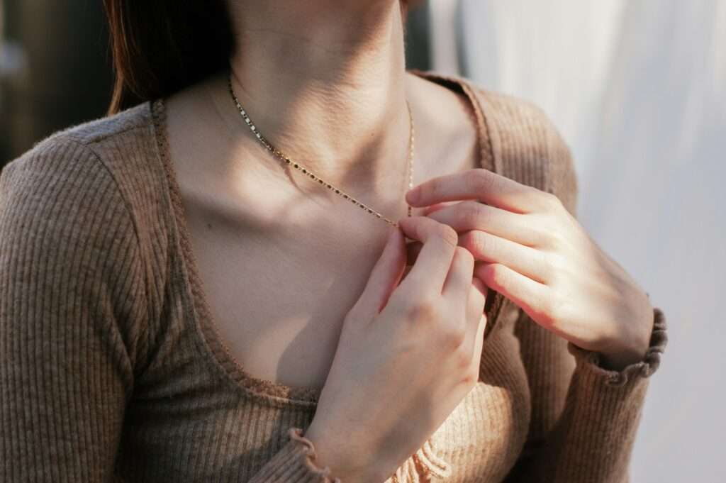 a woman wearing a necklace and holding her hands together